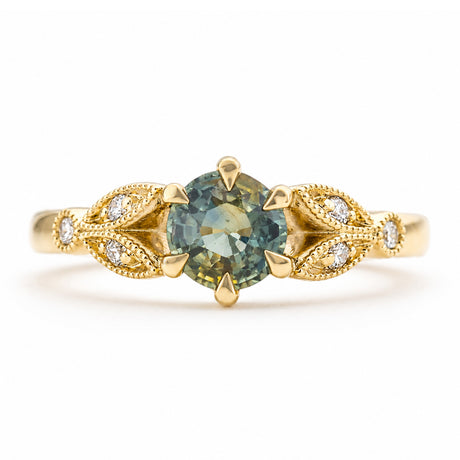 A vintage-inspired, yellow gold engagement ring featuring a central round-cut blue-green sapphire in a prong setting, flanked by decorative leaf-shaped pavé settings with diamond accent stones, shown on a white background.