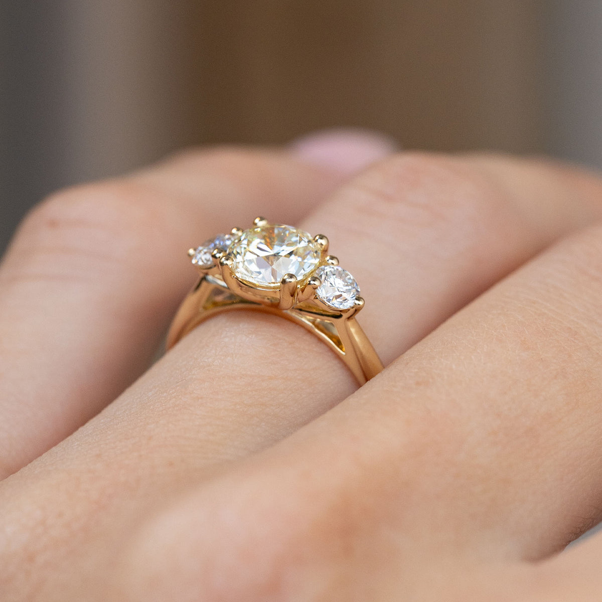 Side-angle view of the three-stone engagement ring worn on a hand, highlighting the intricate gold setting.