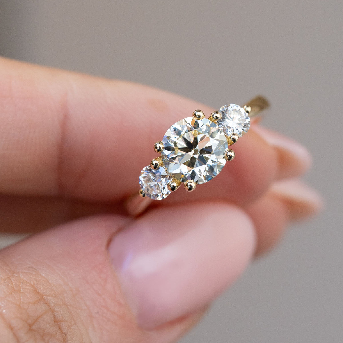 Hand-held close-up of the pale yellow oval diamond flanked by two brilliant-cut white diamonds.