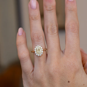 Yellow diamond cluster engagement ring worn on a hand, showcasing its elegant oval shape and delicate gold band.