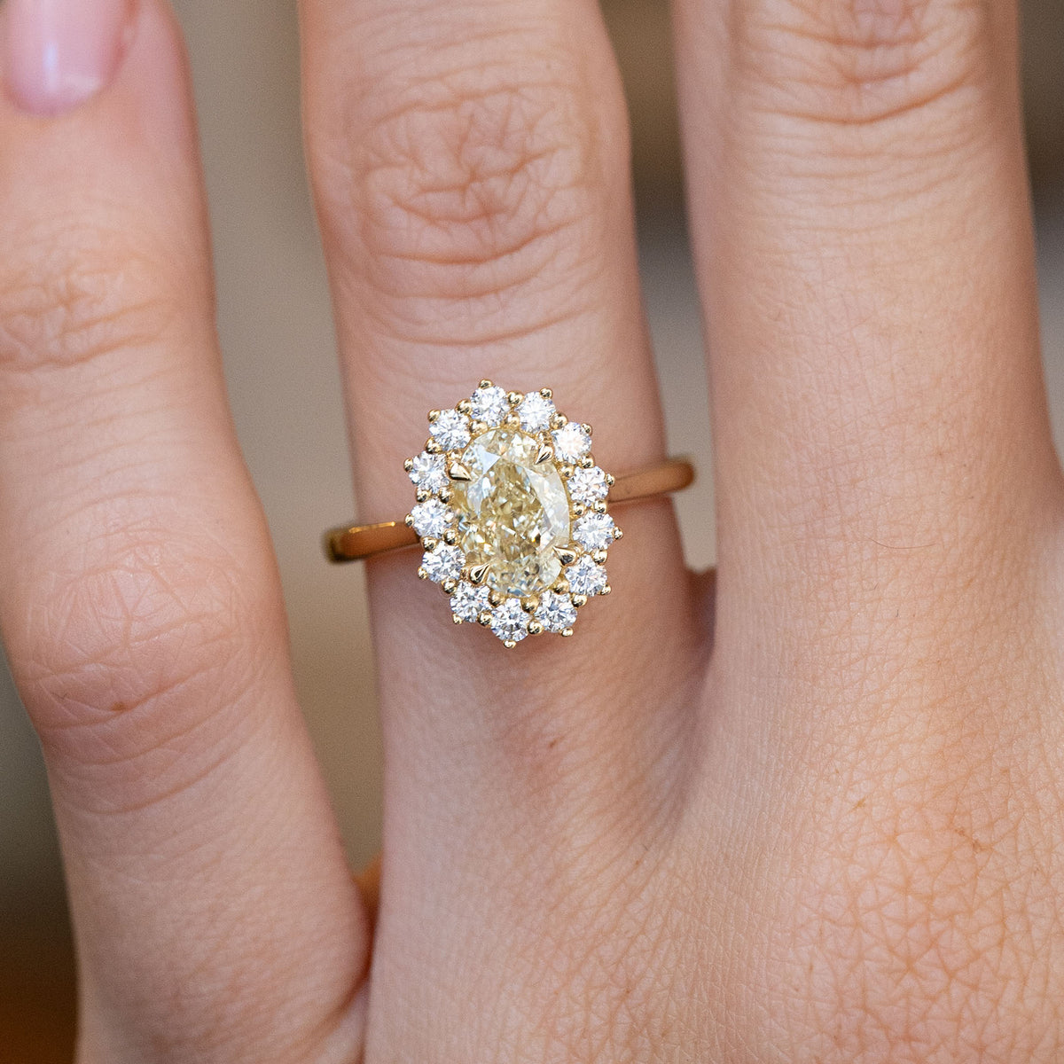 Close-up of the oval yellow diamond engagement ring on a finger, featuring a sparkling cluster of white diamonds.