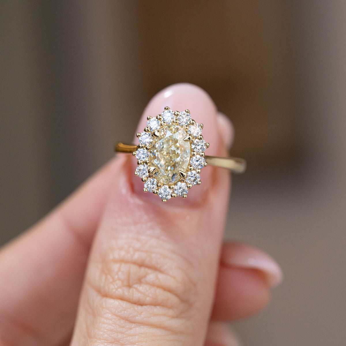Hand-held close-up of the oval yellow diamond surrounded by brilliant-cut white diamonds in a floral-inspired cluster setting.