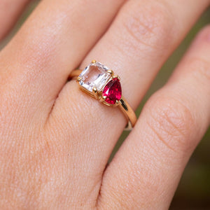 A close-up of a gold Antique-inspired, Pink sapphire and spinel two stone engagement ring worn on a finger.