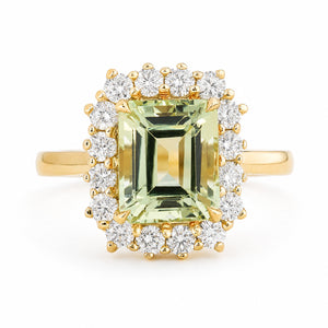 A Vintage-inspired, yellow gold halo engagement ring featuring a large emerald-cut light green beryl surrounded by a row of diamonds, set against a plain white background.
