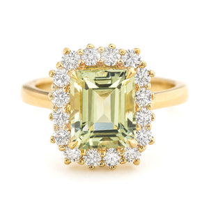 A yellow gold vintage-inspired cluster engagement ring featuring a large emerald-cut pale green beryl surrounded by a halo of diamonds, set against a plain white background.