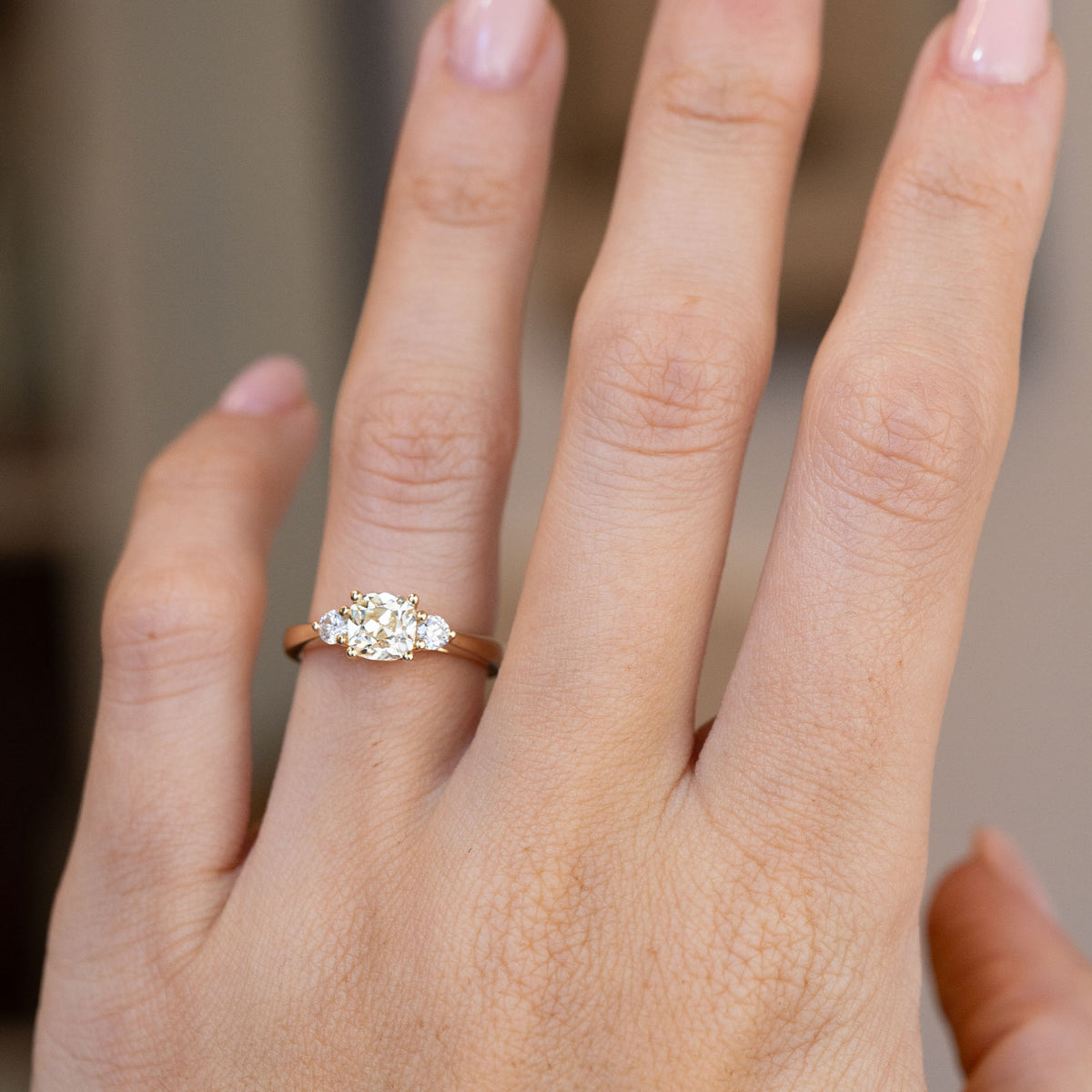 Three-stone diamond engagement ring worn on a hand, showcasing its elegant proportions and classic design.