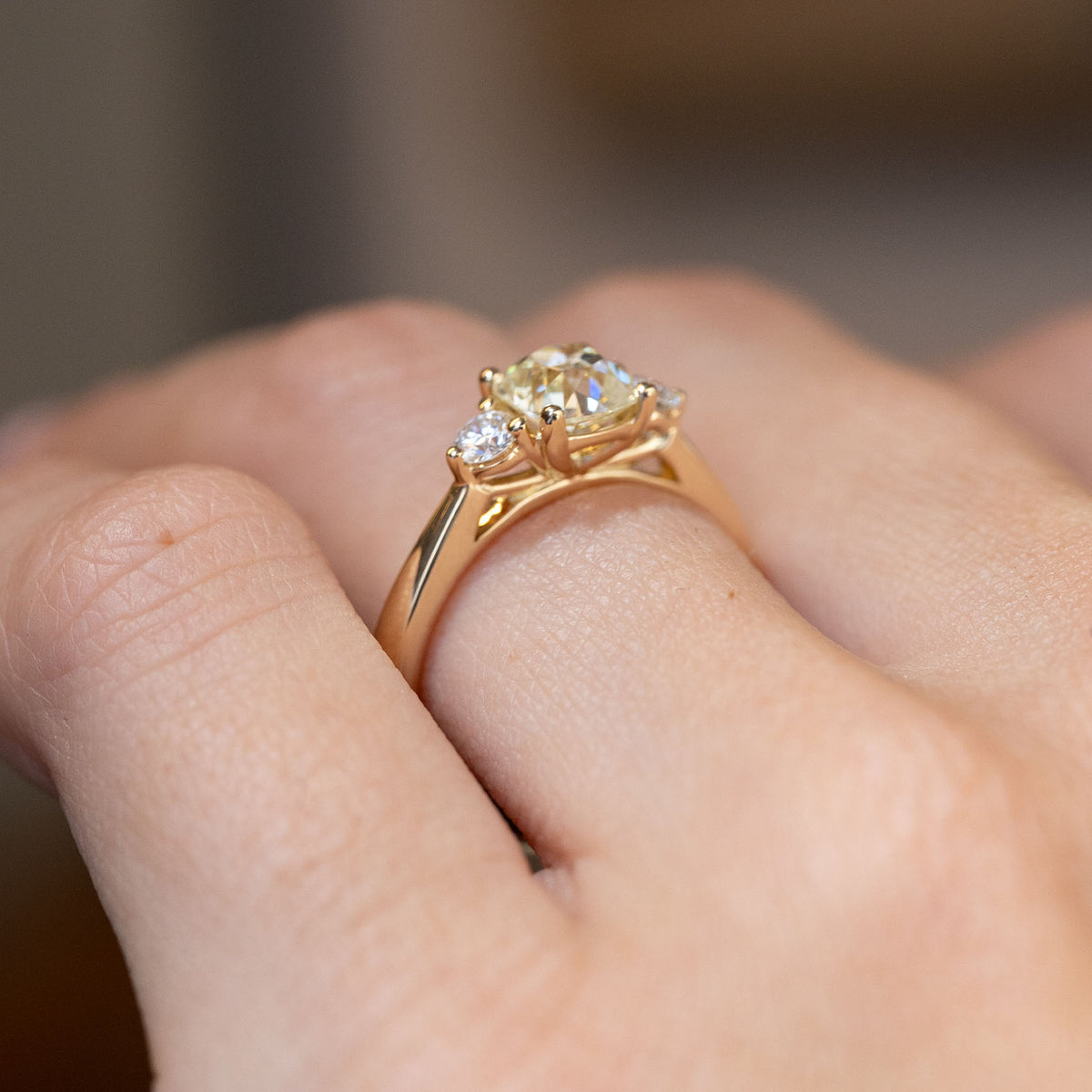 Side-angle view of the diamond engagement ring worn on a hand, highlighting the intricate gallery and raised gold setting.