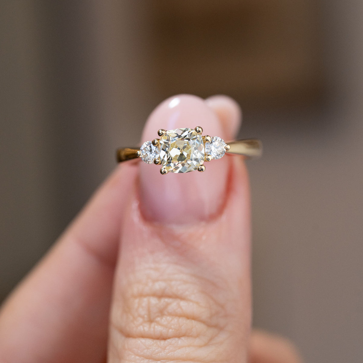 Hand-held close-up of the cushion-cut centre diamond with sparkling round diamond shoulders in yellow gold.