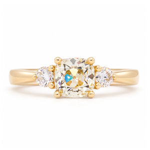 Antique-inspired cushion-cut diamond three-stone engagement ring in yellow gold, featuring two round brilliant-cut diamond shoulders.