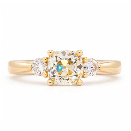 Antique-inspired cushion-cut diamond three-stone engagement ring in yellow gold, featuring two round brilliant-cut diamond shoulders.