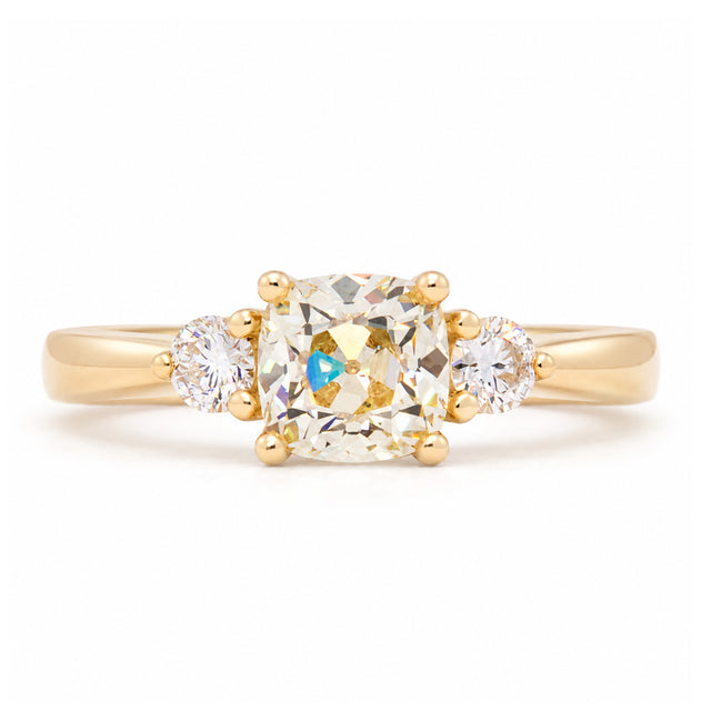 Antique-inspired cushion-cut diamond three-stone engagement ring in yellow gold, featuring two round brilliant-cut diamond shoulders.