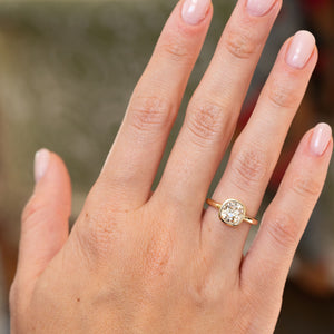 Antique-inspired yellow diamond solitaire ring worn on the hand, showcasing its cushion shape and slender yellow gold band.