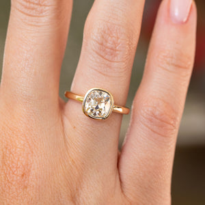 Close-up of an antique-inspired cushion diamond solitaire in yellow gold, featuring a warm yellow tint and softly rounded setting.