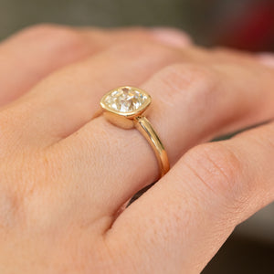 Angled hand view of an antique-style yellow-tinted diamond engagement ring, revealing the raised rub-over setting and tapered band.