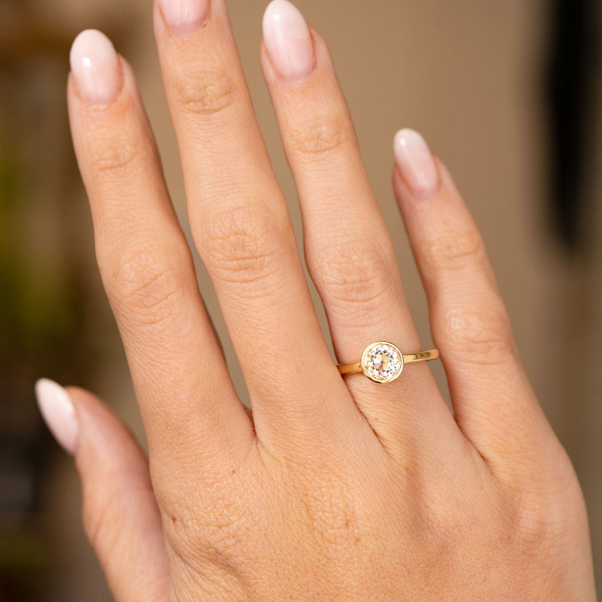 An Antique-inspired, Old-cut diamond solitaire engagement ring set in yellow gold worn on an outstretched hand.