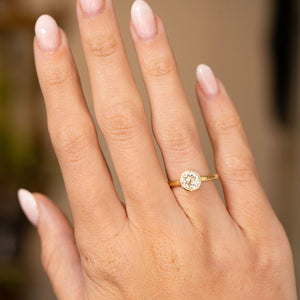 An Antique-inspired, Old-cut diamond solitaire engagement ring set in yellow gold worn on an outstretched hand.
