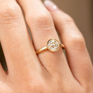 A detailed image of an Antique-inspired, Old-cut diamond solitaire engagement ring in yellow gold worn on a finger in soft natural daylight