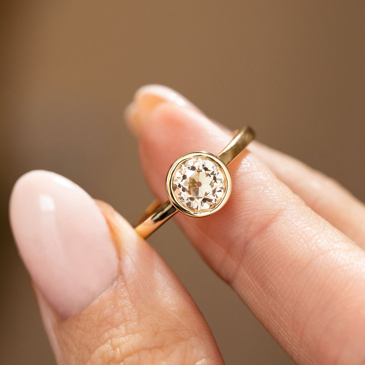 an Antique-inspired, Old-cut diamond solitaire gold engagement ring balanced on a finger and shown up close to display the clarity of the diamond.