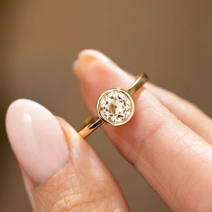 an Antique-inspired, Old-cut diamond solitaire gold engagement ring balanced on a finger and shown up close to display the clarity of the diamond.