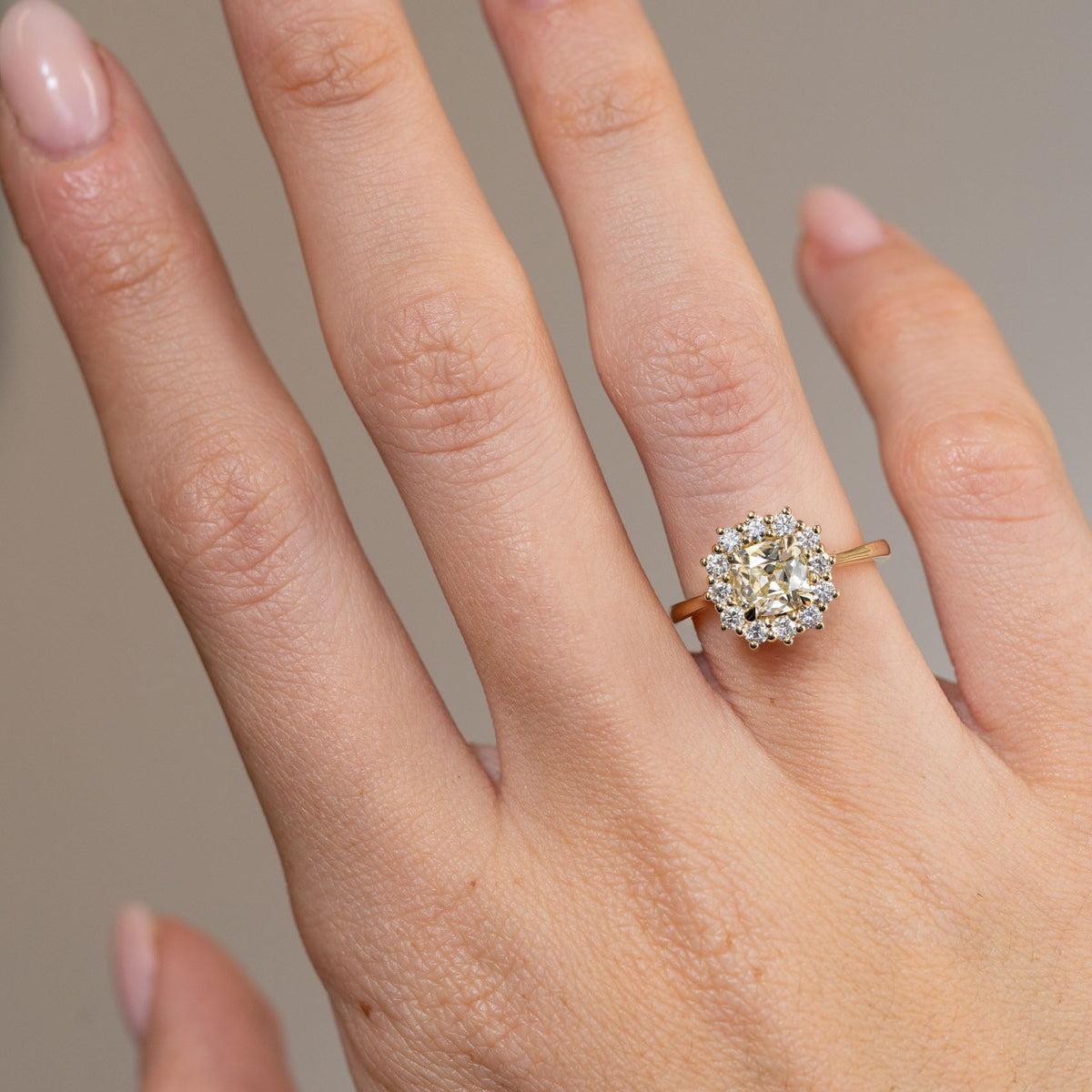 Yellow old-mine cut diamond engagement ring worn on a finger, showcasing its warm champagne tones and antique-inspired cluster design.
