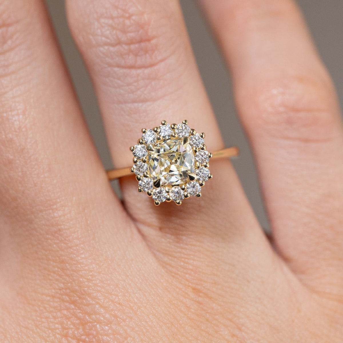 Close-up of the cushion old-mine cut yellow diamond surrounded by brilliant-cut white diamonds, worn on a finger.