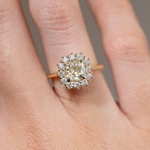 Close-up of the cushion old-mine cut yellow diamond surrounded by brilliant-cut white diamonds, worn on a finger.