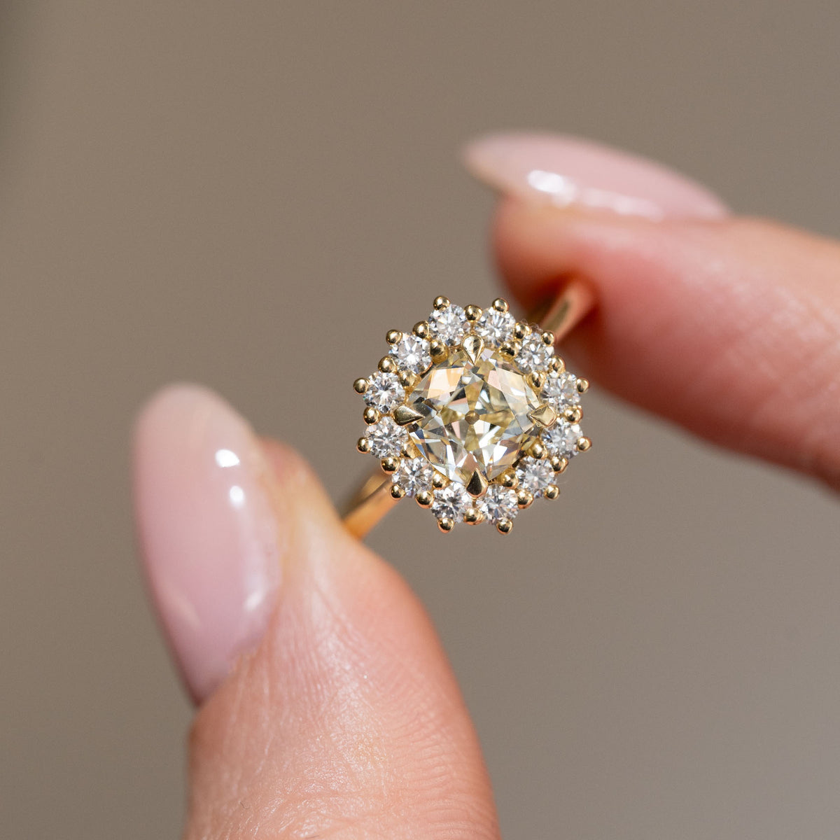 Hand-held close-up of the pale yellow cushion-cut diamond framed by sparkling white diamonds in a classic cluster setting.