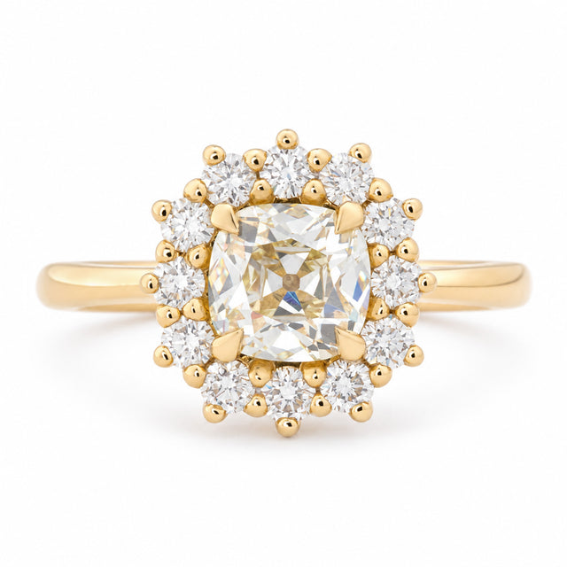 Antique-inspired yellow cushion old-mine cut diamond cluster engagement ring in yellow gold, surrounded by a halo of brilliant-cut white diamonds.