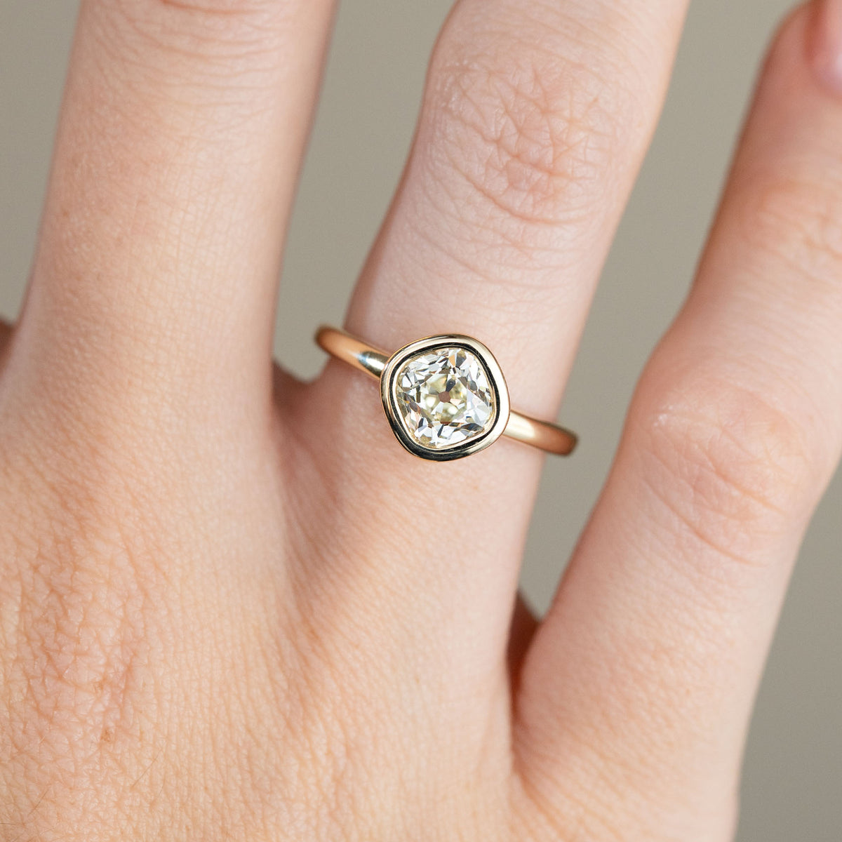 Close-up of the antique-inspired diamond ring on a finger, showing the cushion-shaped centre stone framed by a polished yellow gold bezel.