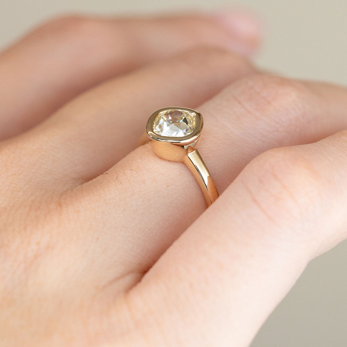 Angled view of the bezel-set diamond engagement ring worn on a hand, displaying its gently raised setting and slim yellow gold shank.
