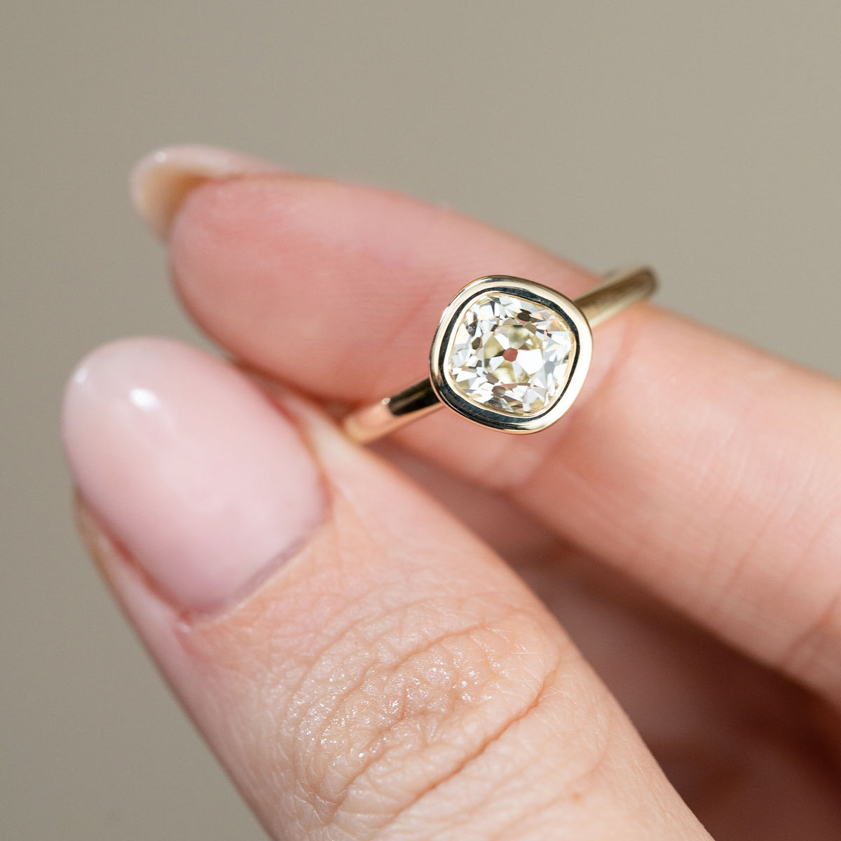Detailed close-up of the old mine-cut diamond ring held between fingertips, emphasising the gemstone's individual facets and softly rounded gold surround.