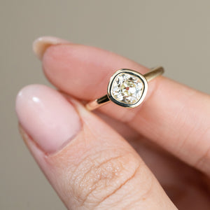 Detailed close-up of the old mine-cut diamond ring held between fingertips, emphasising the gemstone's individual facets and softly rounded gold surround.
