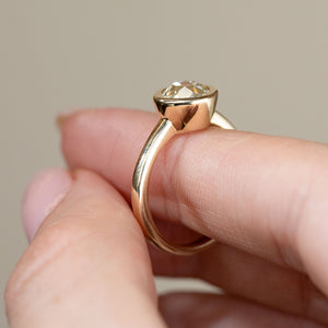 Side profile of the antique-style solitaire ring held between fingers, revealing the smooth elevated bezel setting and gracefully curved yellow gold band.