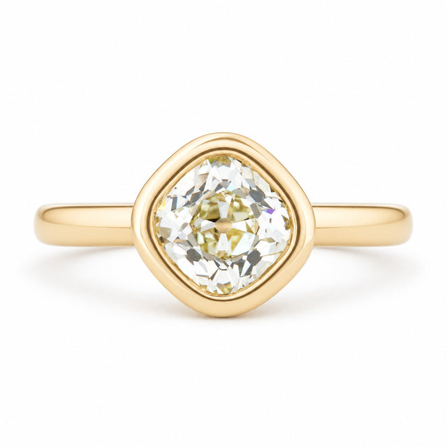 An antique-inspired solitaire engagement ring featuring an old mine-cut diamond in a rounded yellow gold bezel setting.