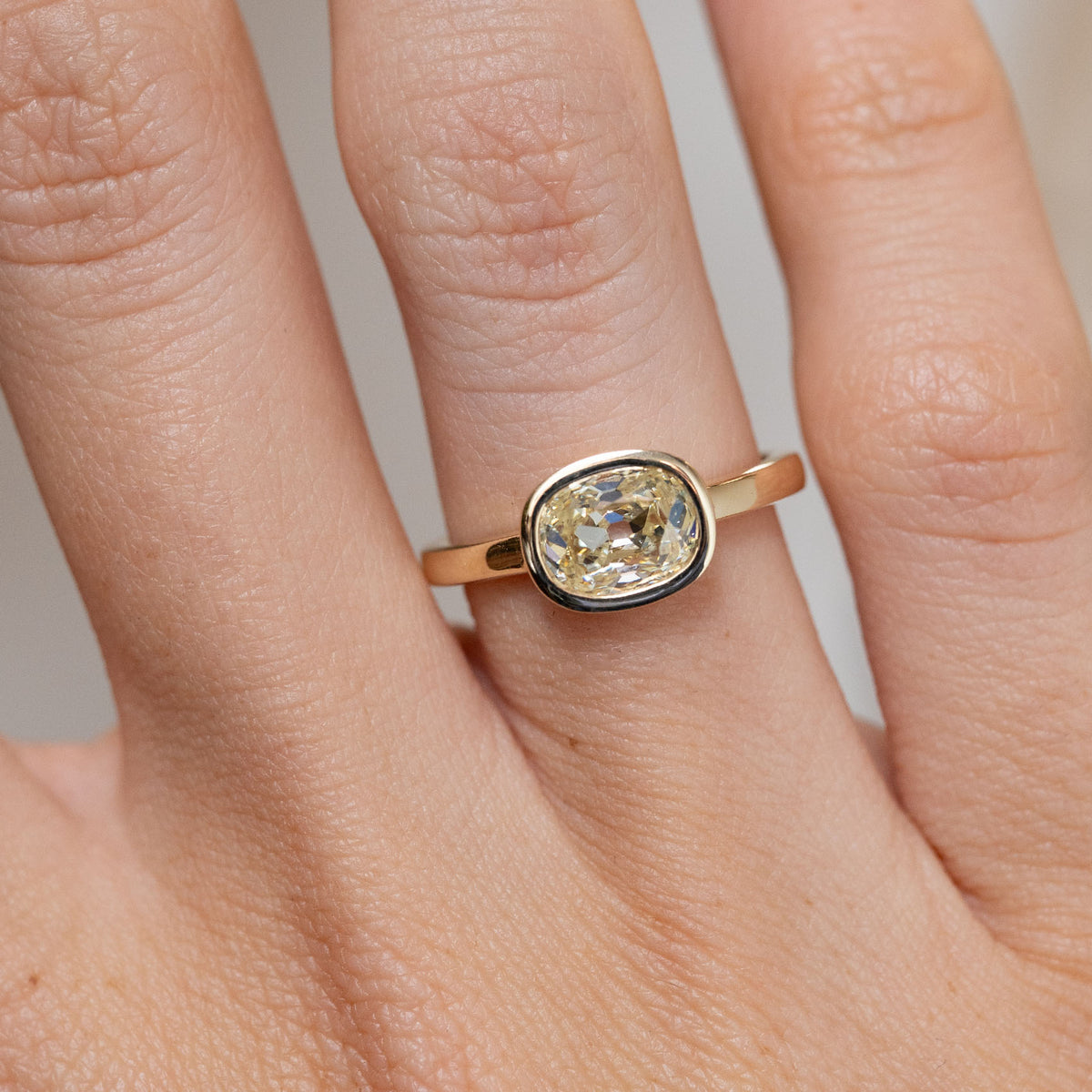 Close-up of the antique-inspired diamond solitaire ring on a finger, featuring a cushion-shaped diamond in a smooth gold bezel.