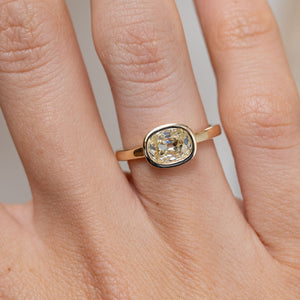 Close-up of the antique-inspired diamond solitaire ring on a finger, featuring a cushion-shaped diamond in a smooth gold bezel.
