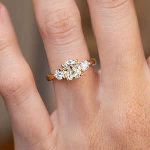 Three-stone engagement ring worn on the hand, showing its warm central diamond.