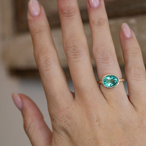 Sea-green beryl solitaire engagement ring worn on a hand, showcasing its vibrant turquoise-green colour and minimalist design.
