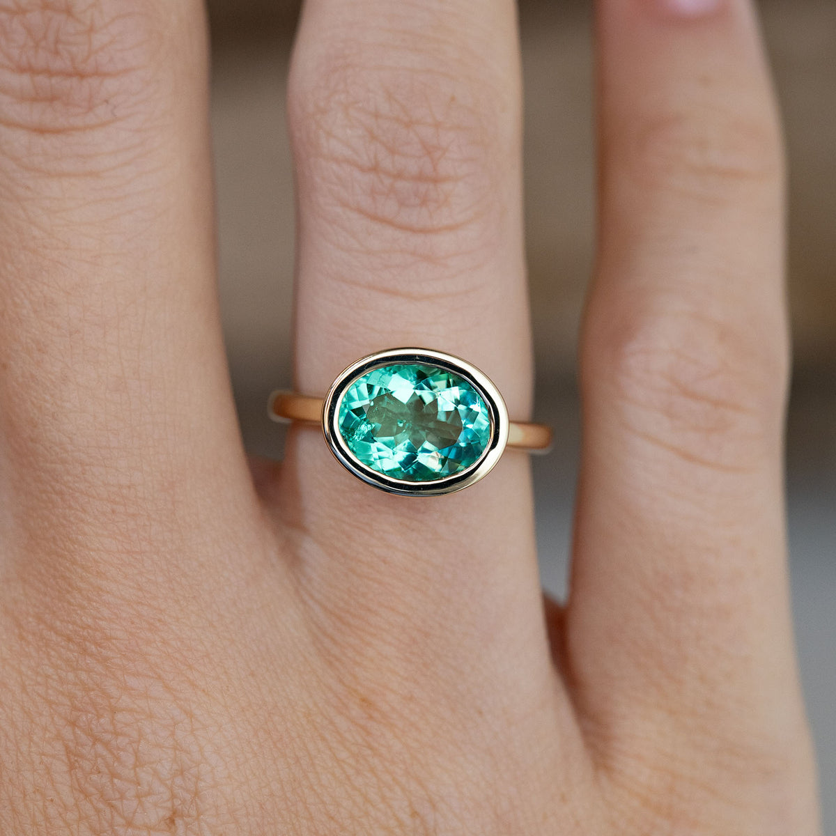 Close-up of the sea-green oval beryl gemstone in a polished yellow gold bezel setting, worn on a finger.