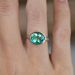Close-up of the sea-green oval beryl gemstone in a polished yellow gold bezel setting, worn on a finger.