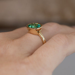 Side-angle view of the sea-green beryl engagement ring worn on a hand, highlighting the smooth bezel setting and delicate 14ct yellow gold band.