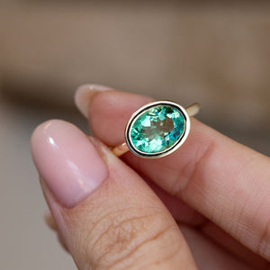 Hand-held close-up of the vibrant oval beryl gemstone, framed by a sleek yellow gold bezel in an antique-inspired solitaire design.
