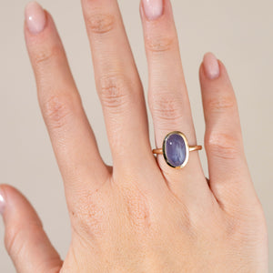 Blue-purple sapphire solitaire worn on a hand, displaying its elegant oval shape and delicate yellow gold setting.