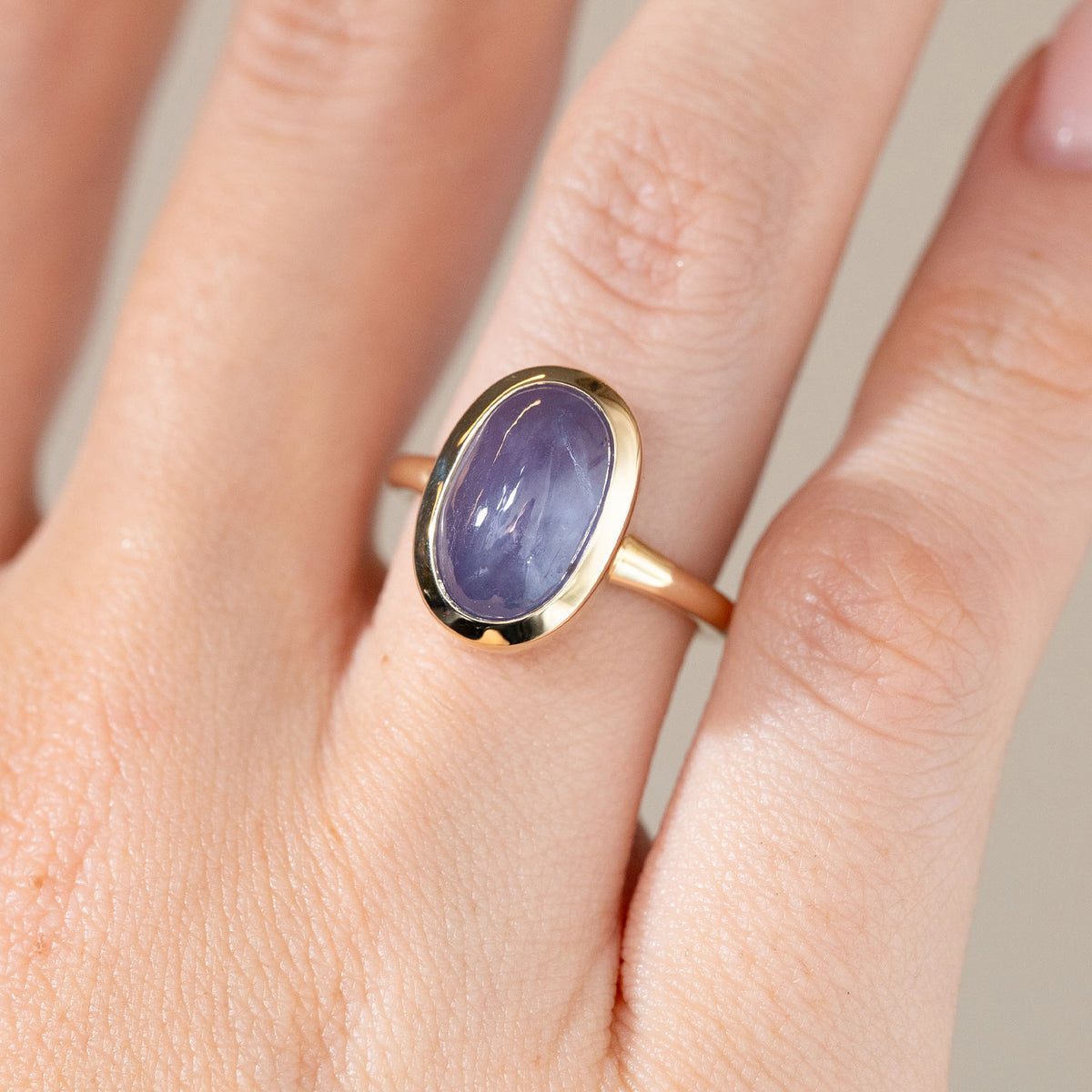 Close-up of the cat's eye sapphire engagement ring on a finger, highlighting its silky purple colour and smooth domed surface.