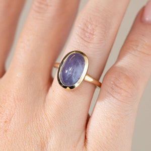 Close-up of the cat's eye sapphire engagement ring on a finger, highlighting its silky purple colour and smooth domed surface.