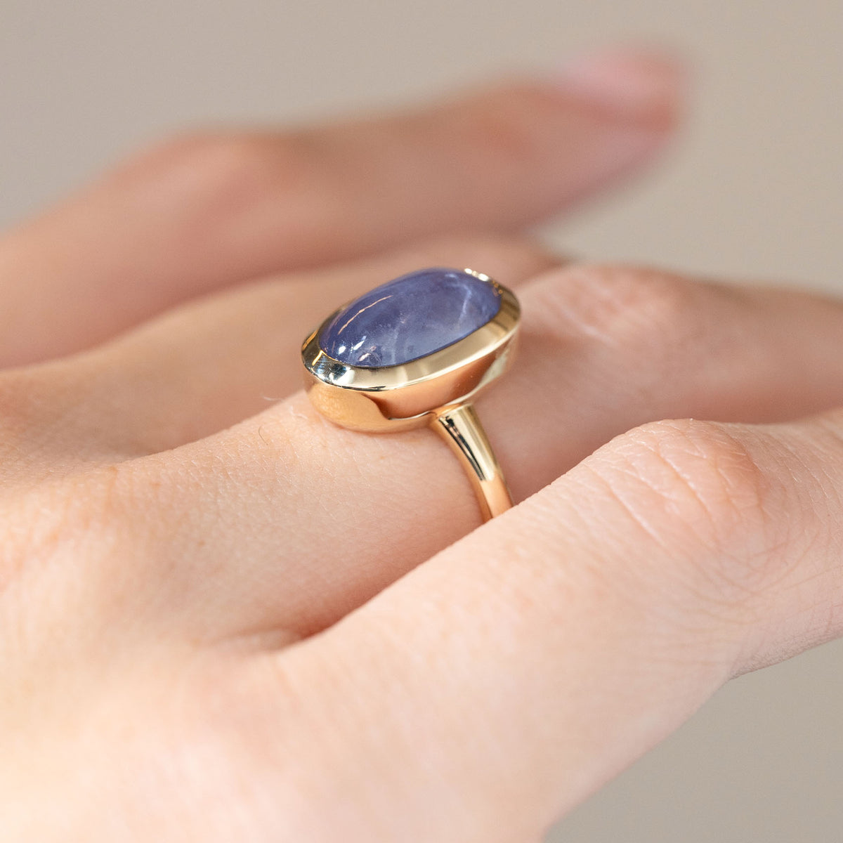 The yellow gold sapphire ring photographed at an angle on a hand, displaying its raised bezel setting and slender band.