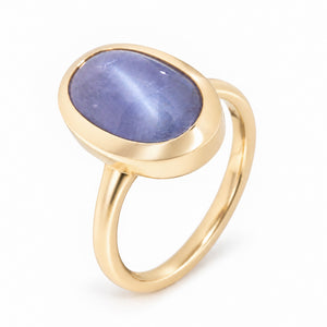 An angled photograph of the sapphire ring, showcasing its soft lavender tones, subtle cat's eye effect and polished gold band.