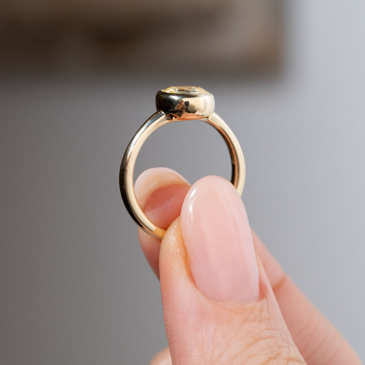 Side profile of an antique-inspired pale yellow sapphire solitaire engagement ring held between fingers, revealing the smooth rounded bezel setting and gently tapered yellow gold band.