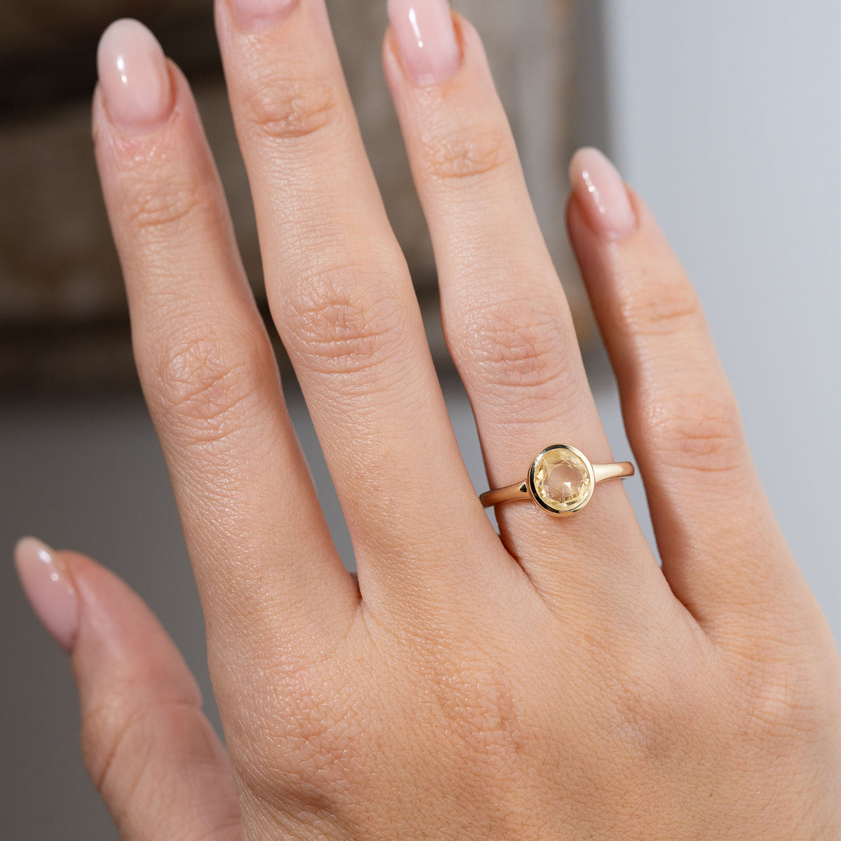 Antique-inspired pale yellow sapphire solitaire engagement ring worn on a hand, showcasing the softly coloured oval sapphire and elegant simplicity of its yellow gold design.