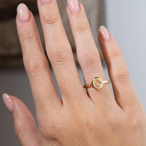 Antique-inspired pale yellow sapphire solitaire engagement ring worn on a hand, showcasing the softly coloured oval sapphire and elegant simplicity of its yellow gold design.